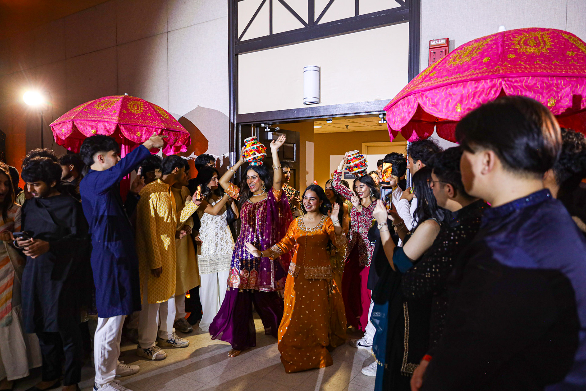 Guests dancing beneath bright pink ceremonial umbrellas at a cultural celebration